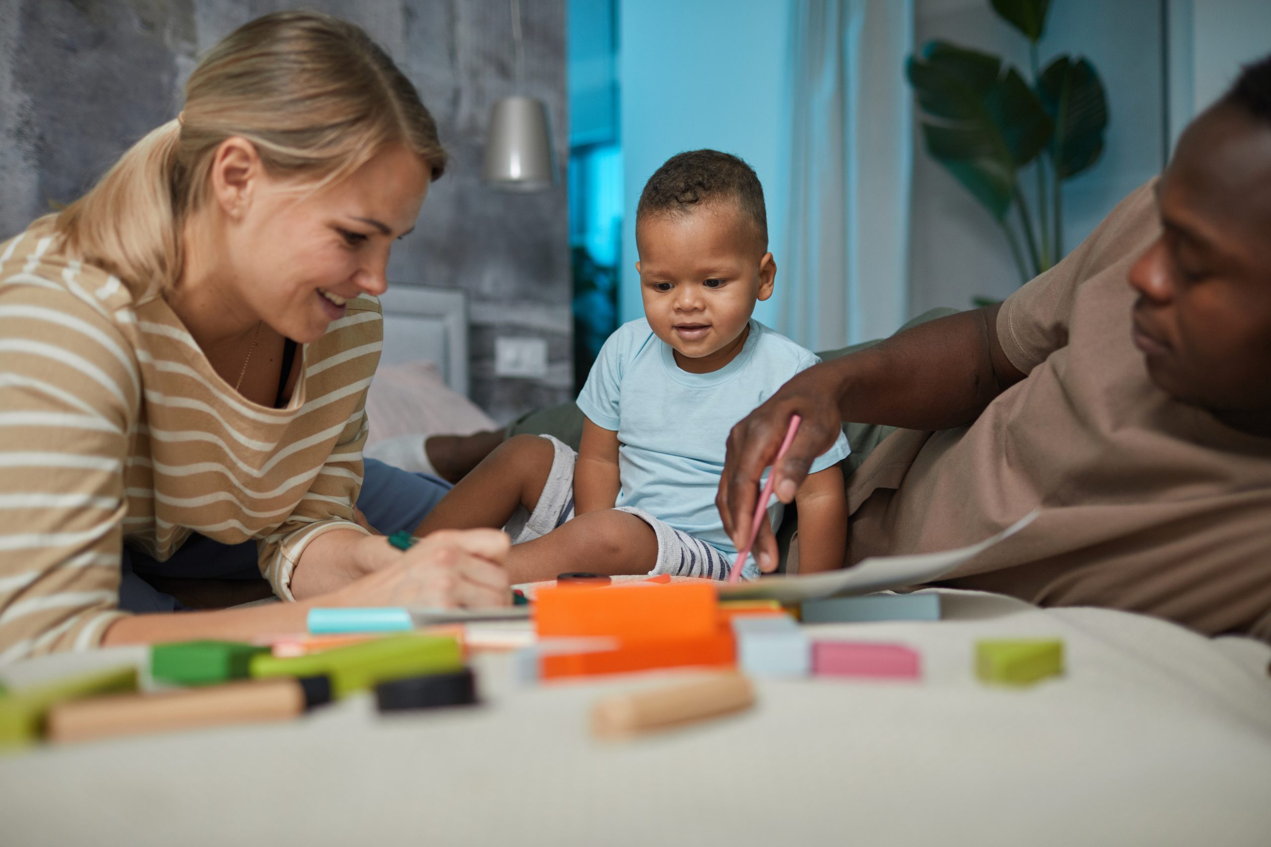Portrait of multiethnic family with cute baby boy playing together while lying on bed at home.